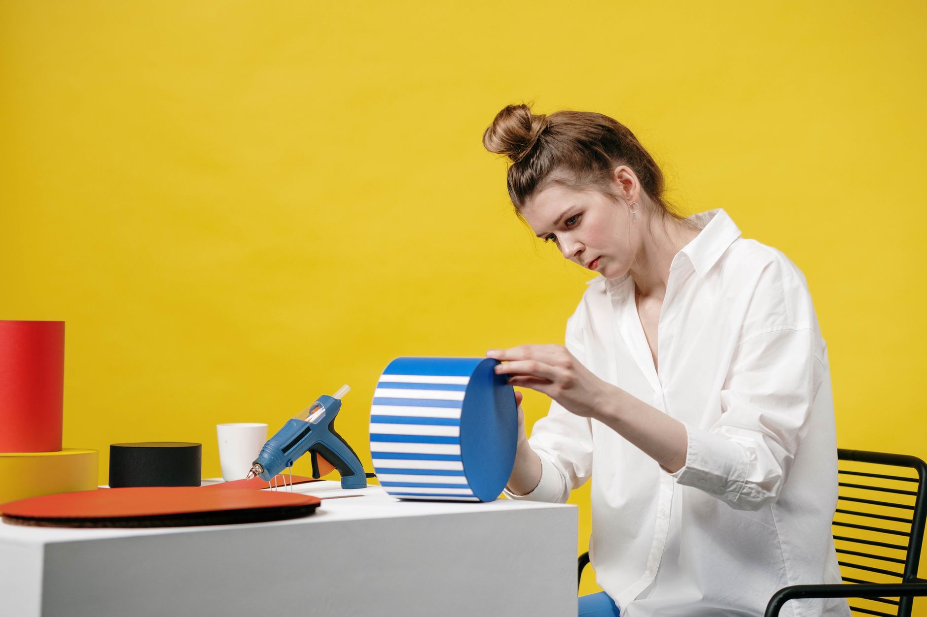 Woman engaged in paper crafting at a vibrant, yellow backdrop studio.