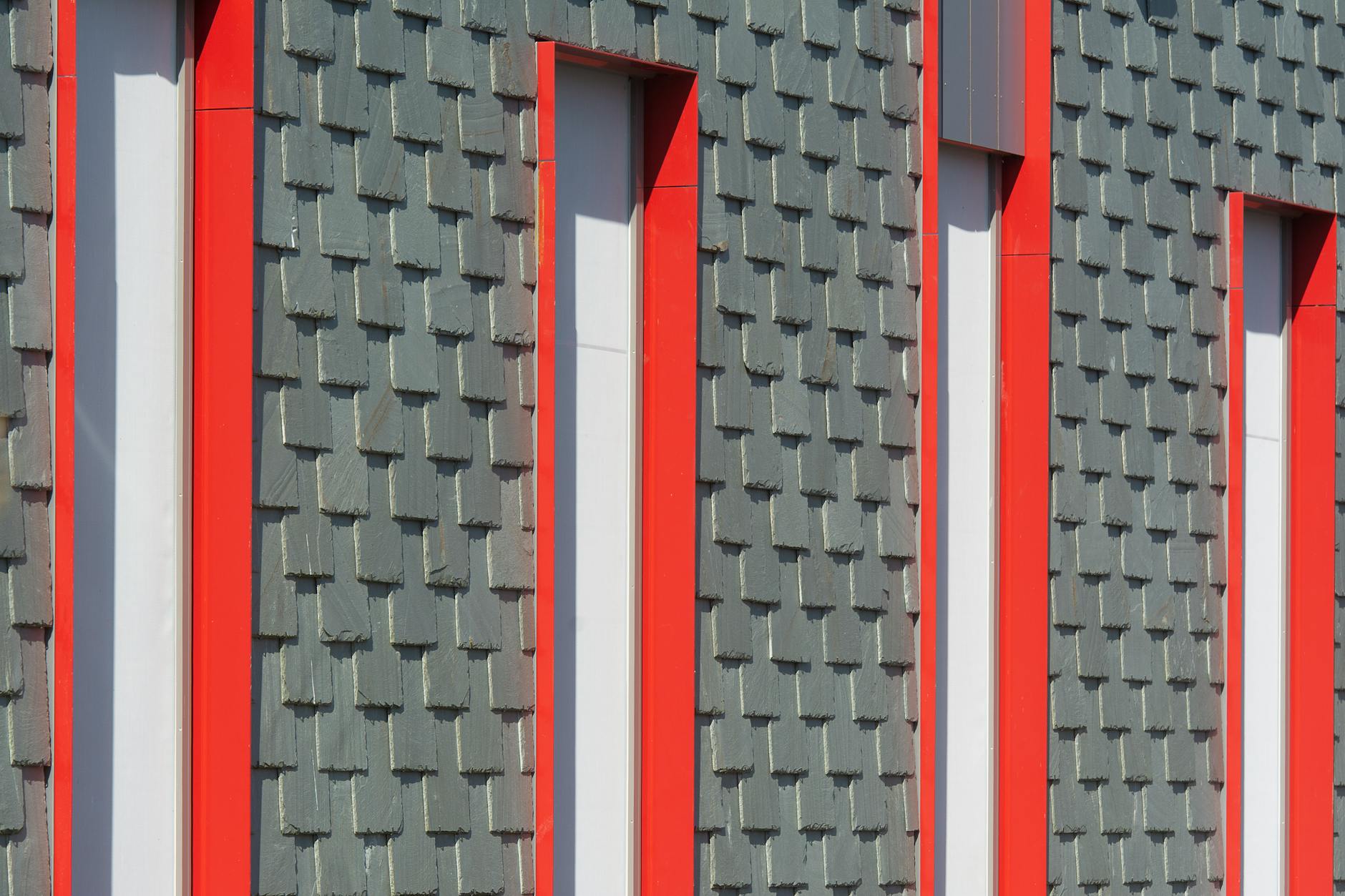 Close-up of a modern building facade with red window frames and textured panels.