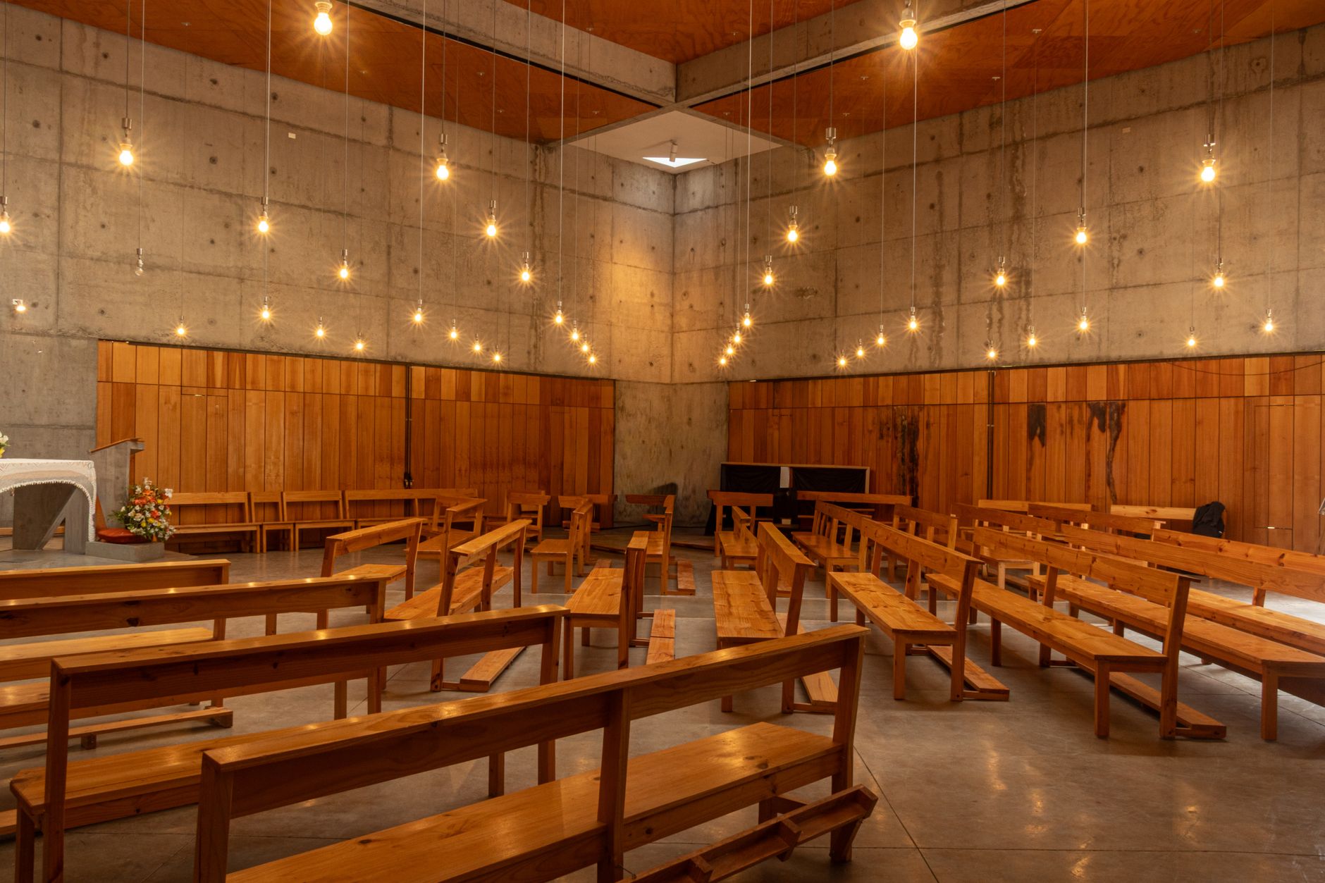Spacious church interior with wooden benches and hanging lights.