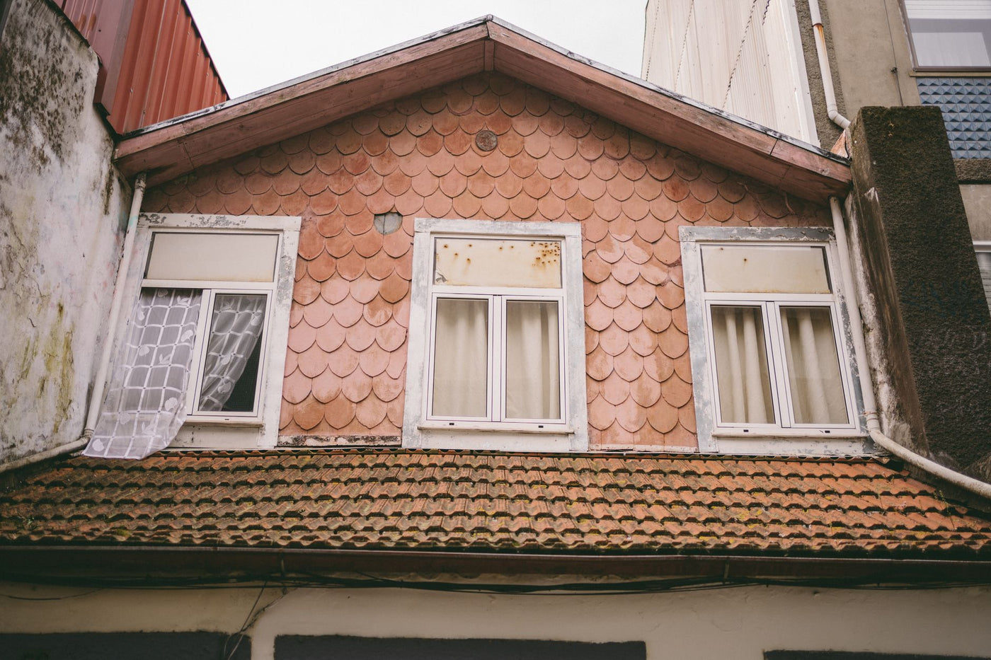 Close-up of a charming attic window with distinctive shingles on a vintage urban building facade.