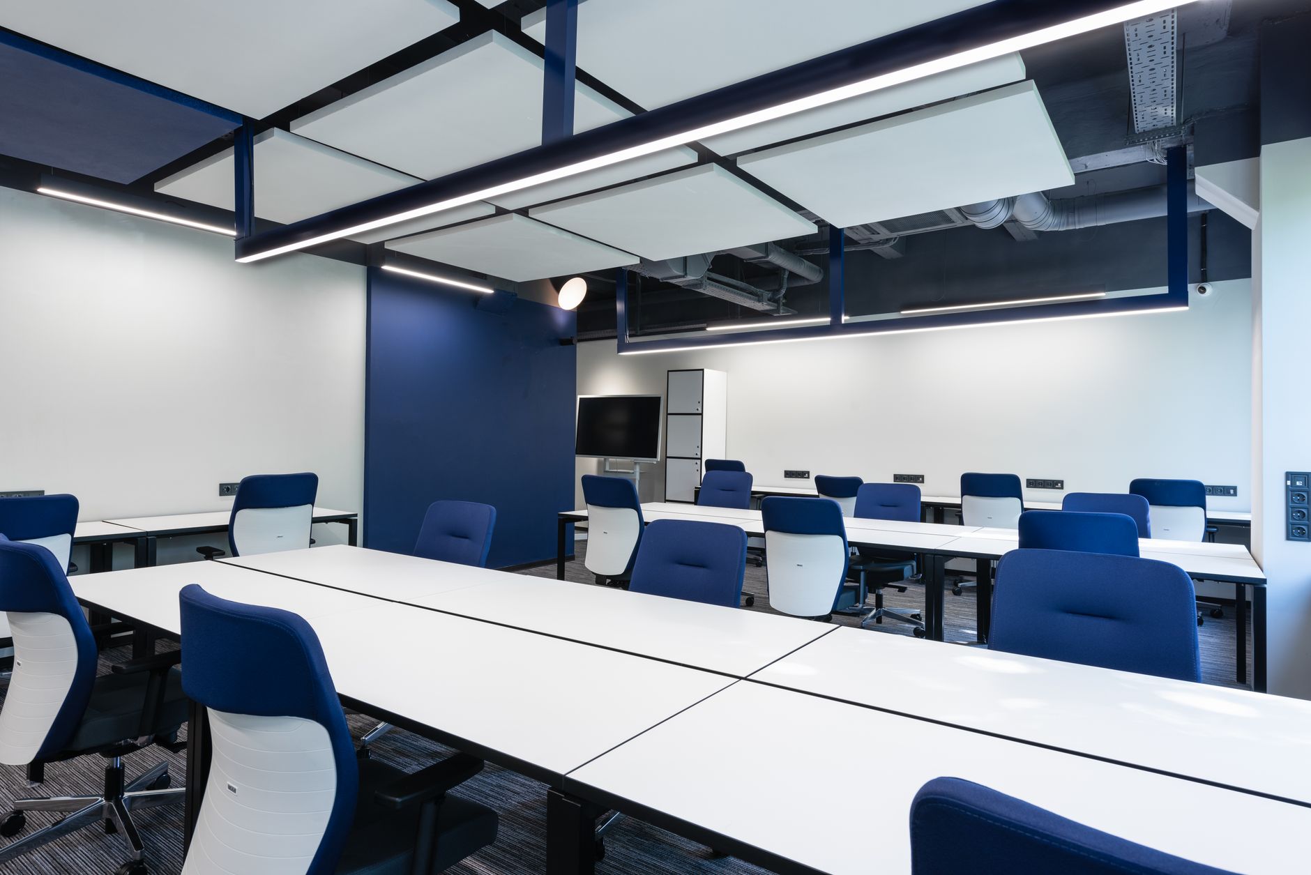 Interior of modern spacious workspace with long white tables and blue armchairs placed near monitor with black screen in business center