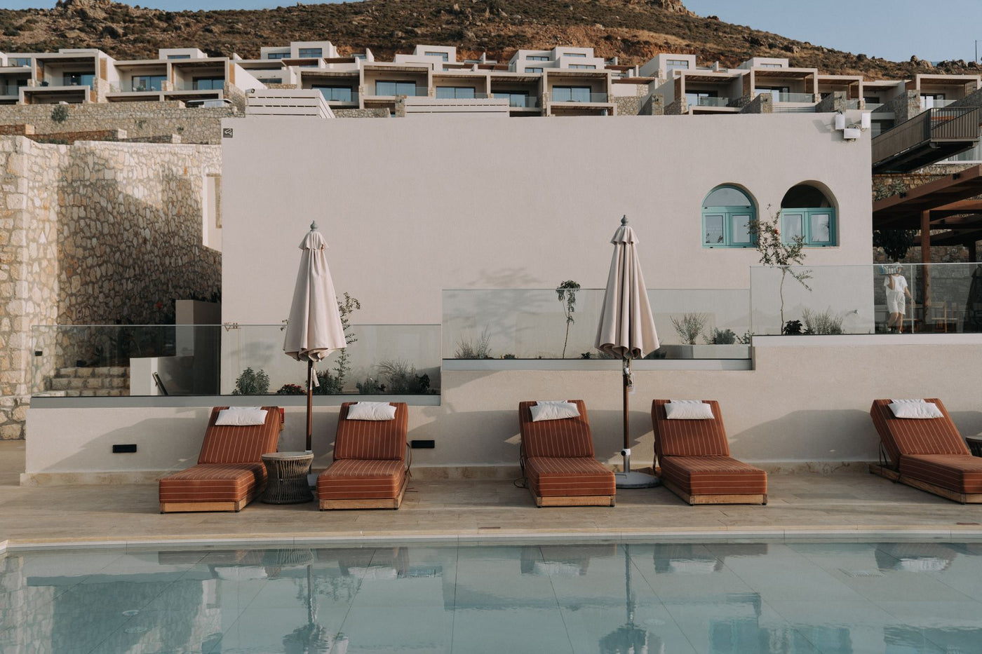 Luxury resort poolside with plush lounge chairs and umbrellas against modern architecture.
