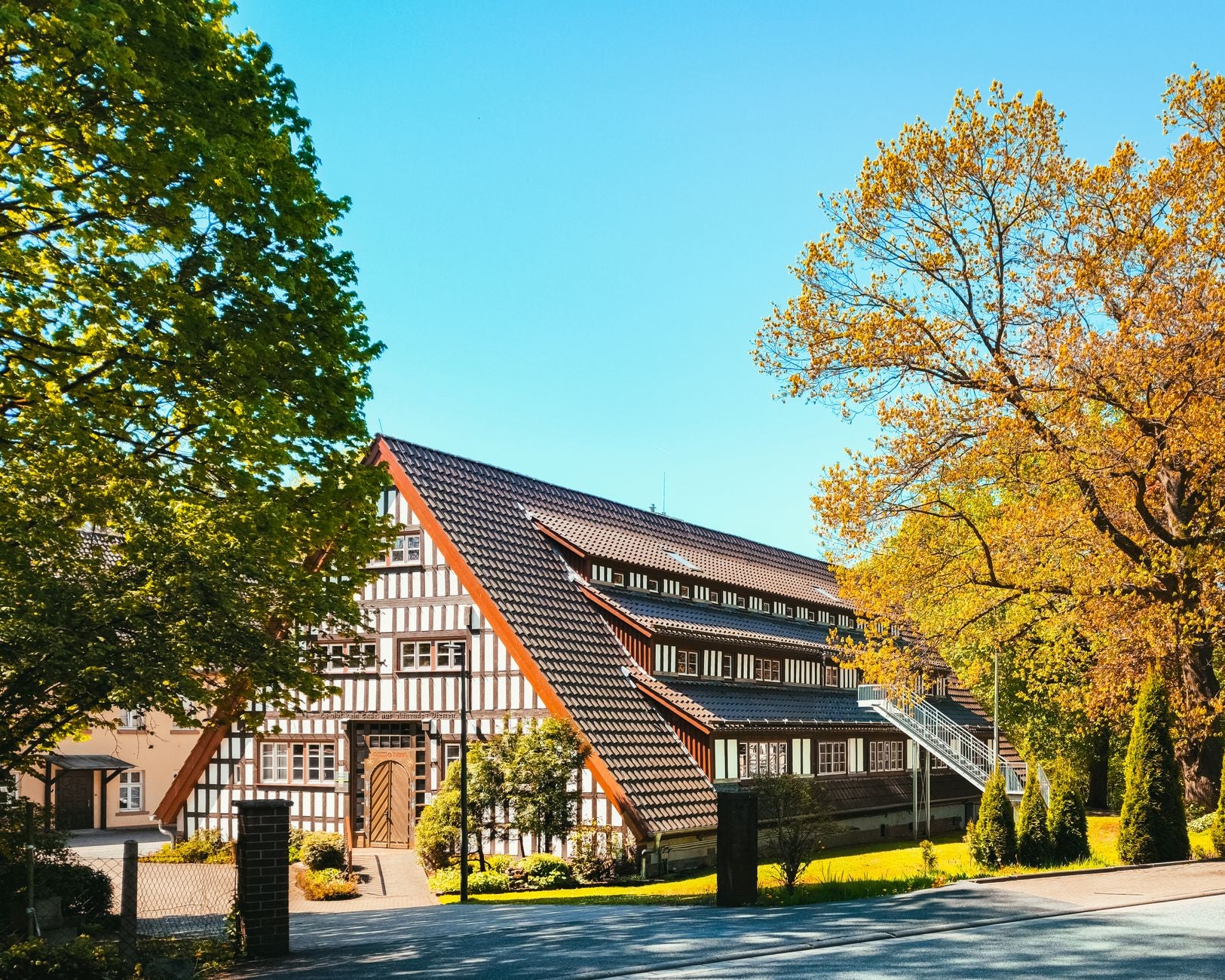 A beautiful half-timbered house surrounded by autumn foliage under a bright blue sky.