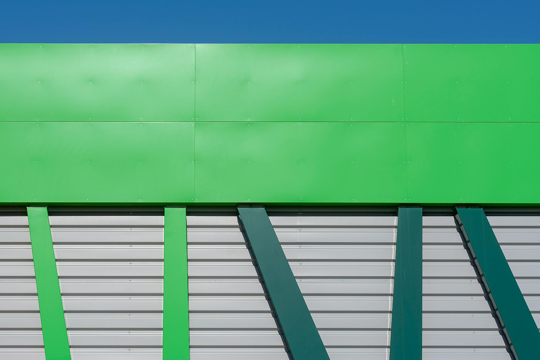 Close-up of a modern green industrial building facade with geometric design against a clear blue sky.