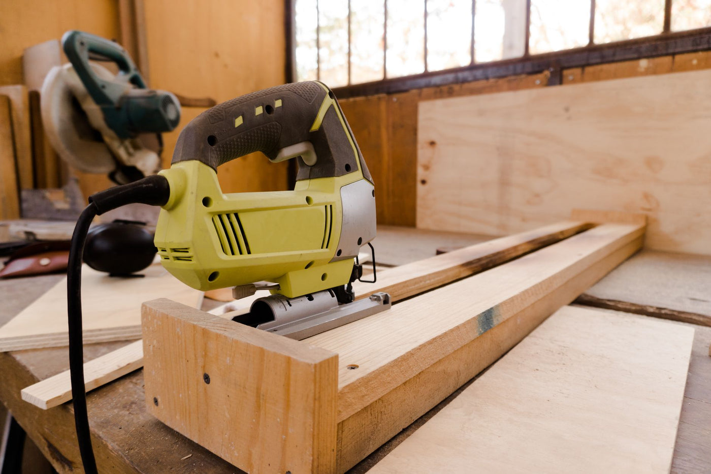 A close-up of an electric jigsaw placed on a wooden workbench in a carpentry workshop.