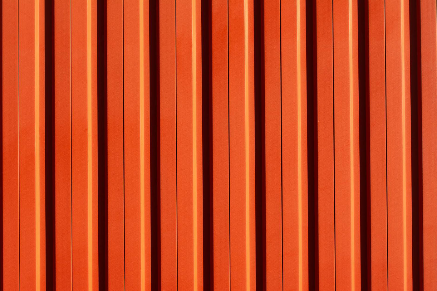 A vivid orange metal wall with vertical stripes, showcasing a modern architectural design.