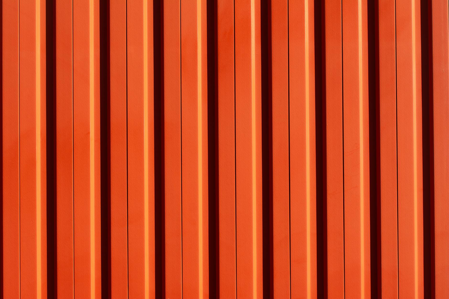 A vivid orange metal wall with vertical stripes, showcasing a modern architectural design.