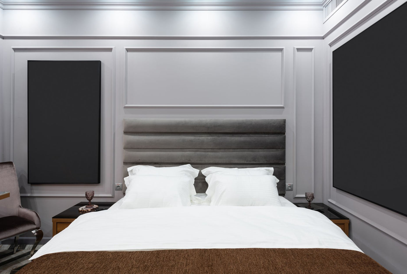 Contemporary bedroom with soft pillows on bed between bedside tables with glasses in light house