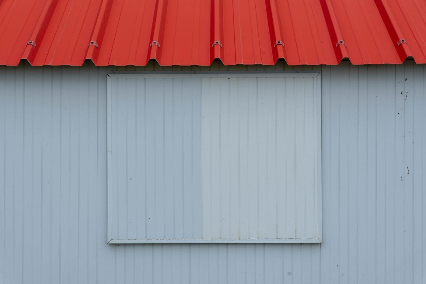Minimalist image of a red metal roof with blue-grey corrugated panel wall.
