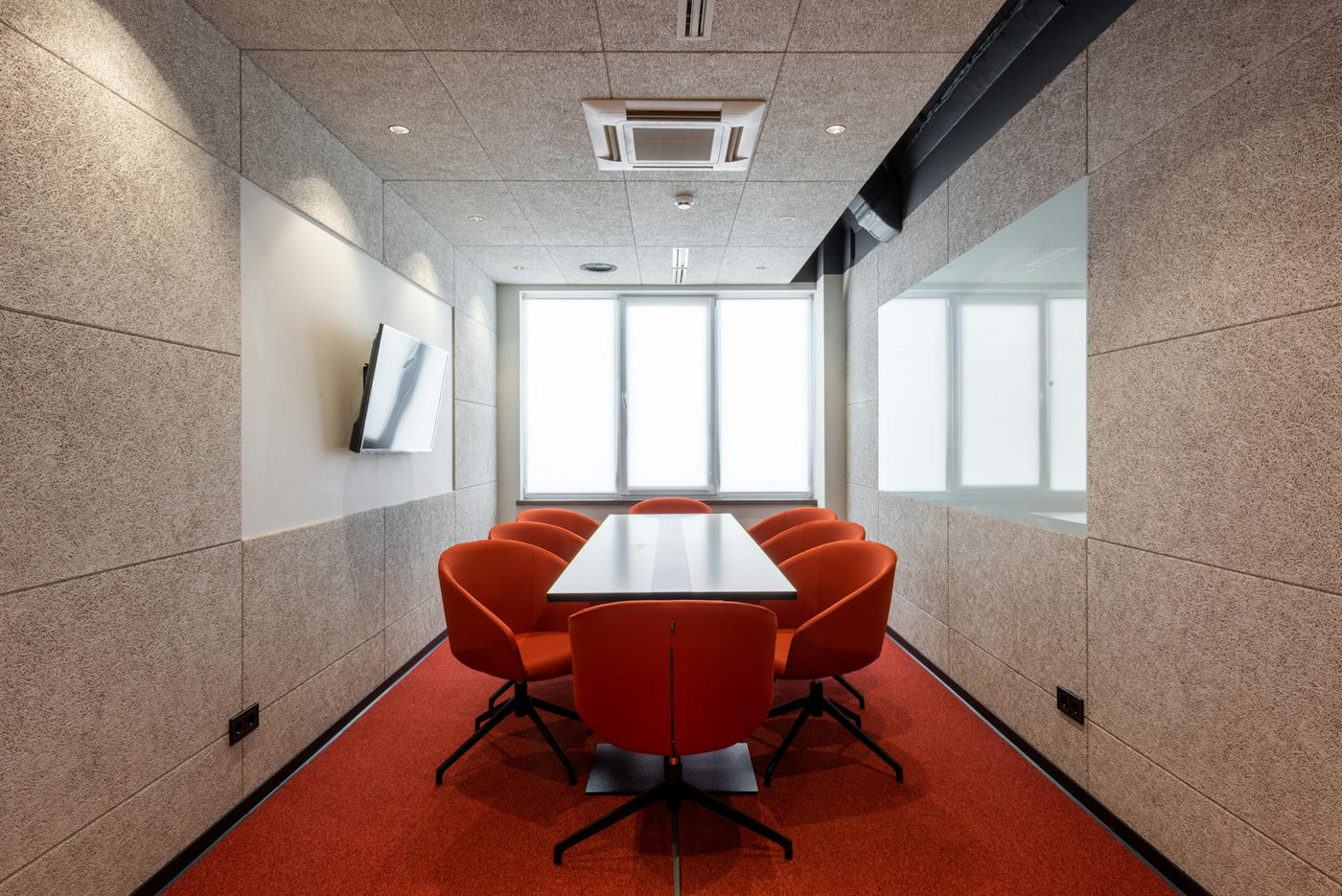 Orange chairs placed around white table in modern conference room with window and TV on wall in contemporary business center