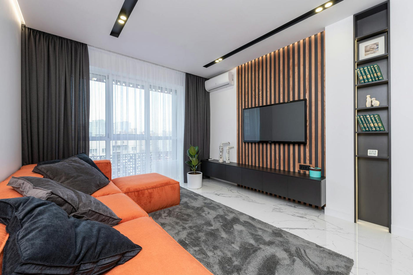 Modern spacious room with window and black cushions on orange couch placed on rug against wall with striped decorations and TV