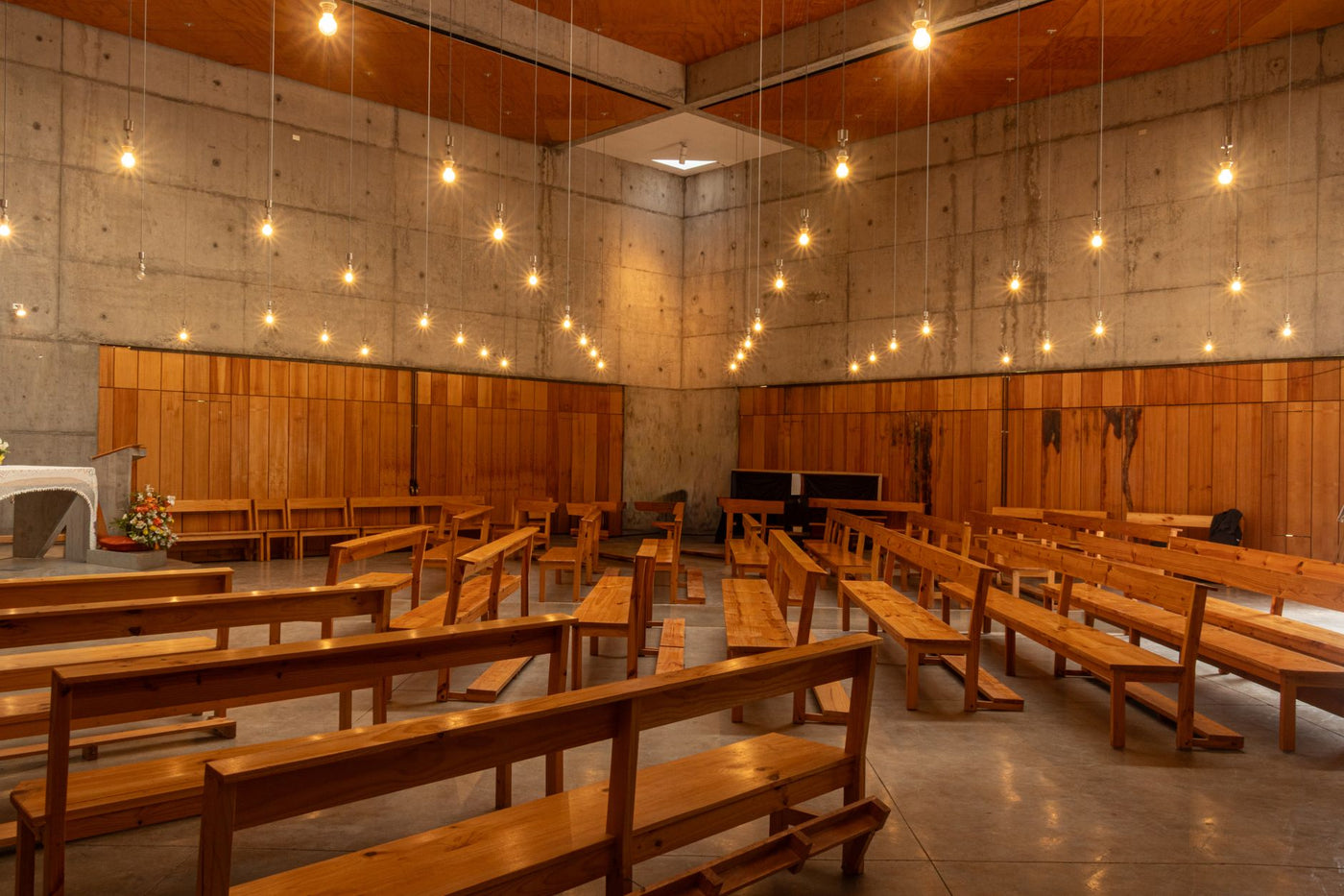 Spacious church interior with wooden benches and hanging lights.